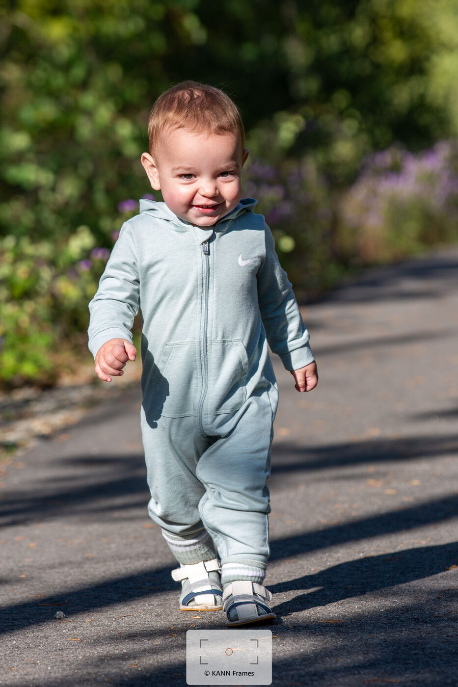 Toddler boy smiling while walking down a garden path